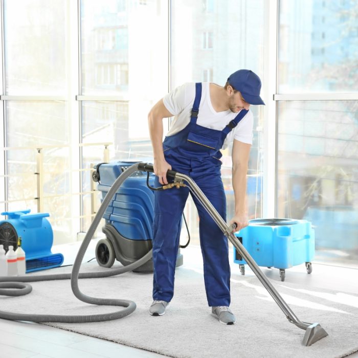 Trabajador de limpieza profesional aspirando un piso amplio y luminoso.