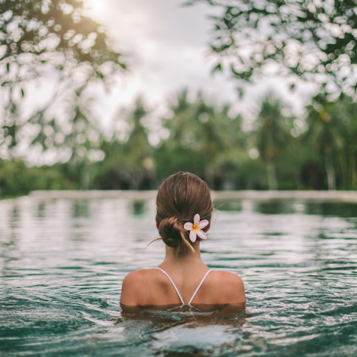 Mujer relajándose en piscina natural con una flor en el cabello, promoviendo Retiro tranquilo Descubrimiento.